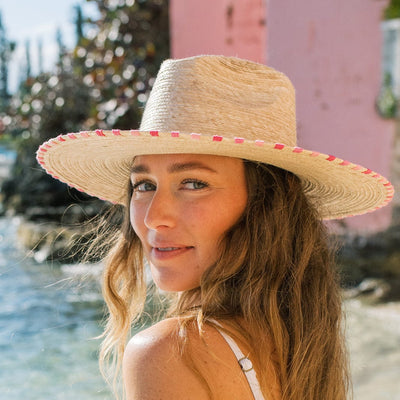 Woman wearing a straw hat with pink trim by a body of water.