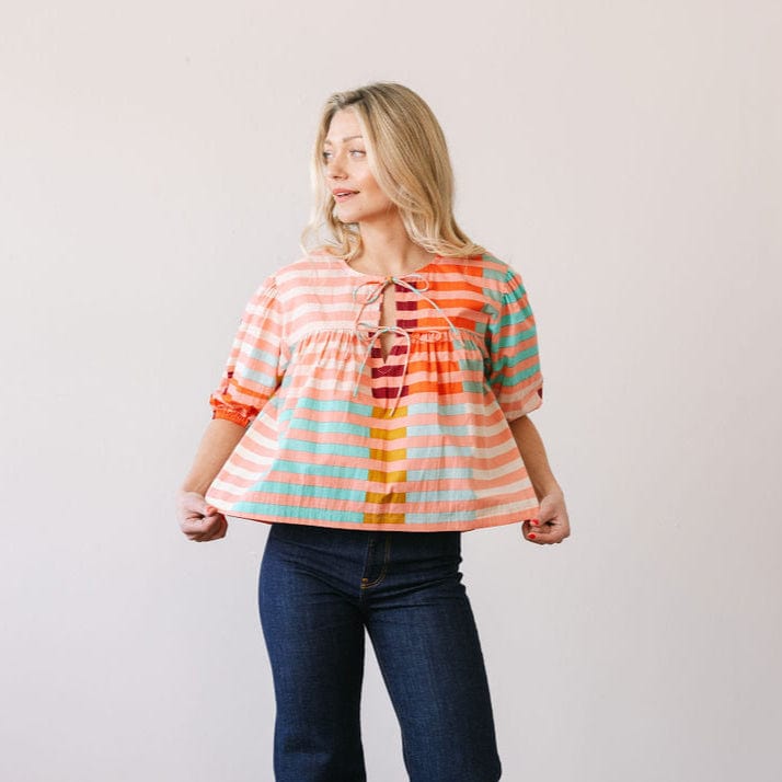Woman wearing a colorful striped blouse and jeans against a plain background