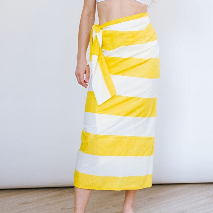 A person standing in front of a white background wearing a yellow and white striped sarong tied around the waist.