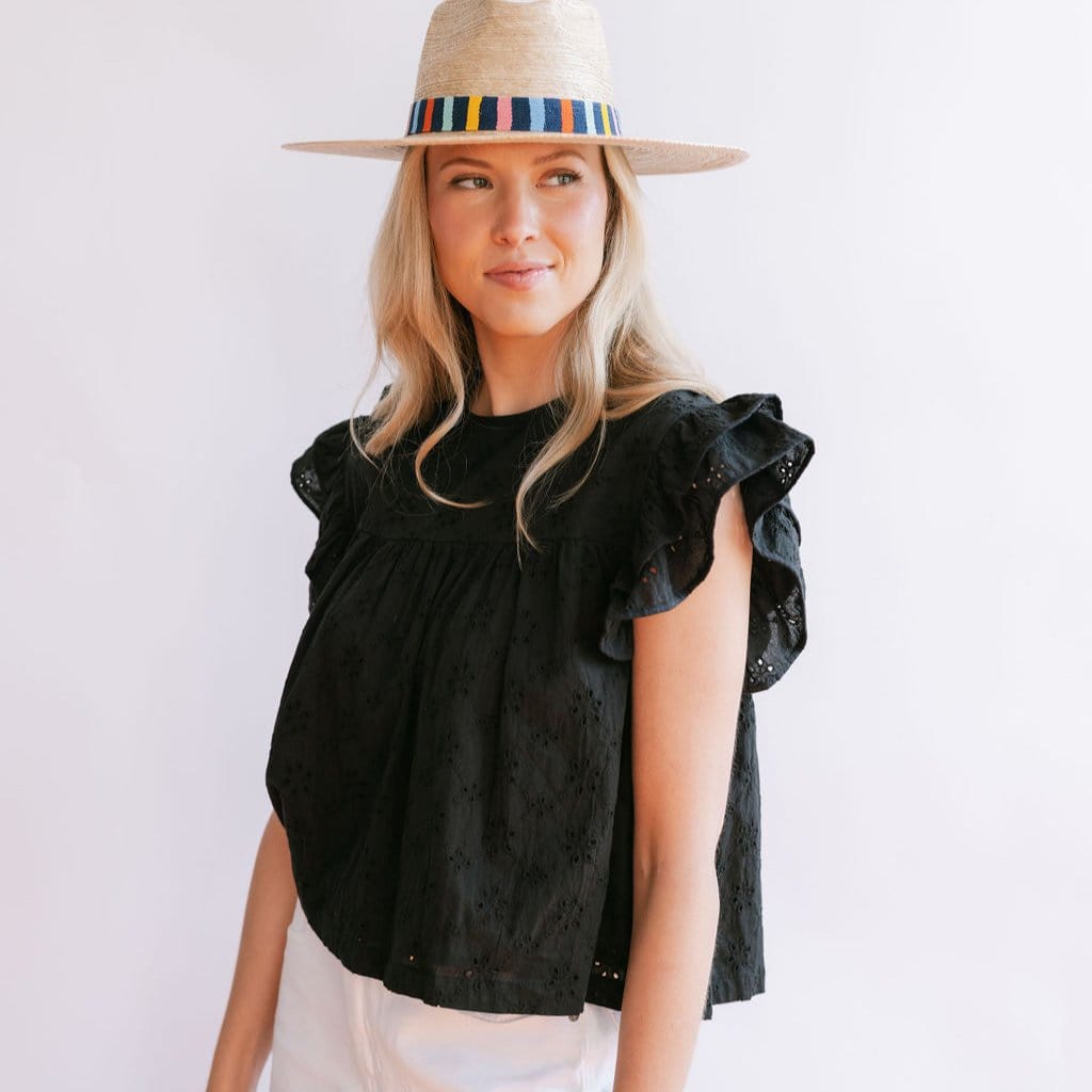 A woman wearing a black eyelet top with flutter sleeves and a straw hat with a multicolored band.