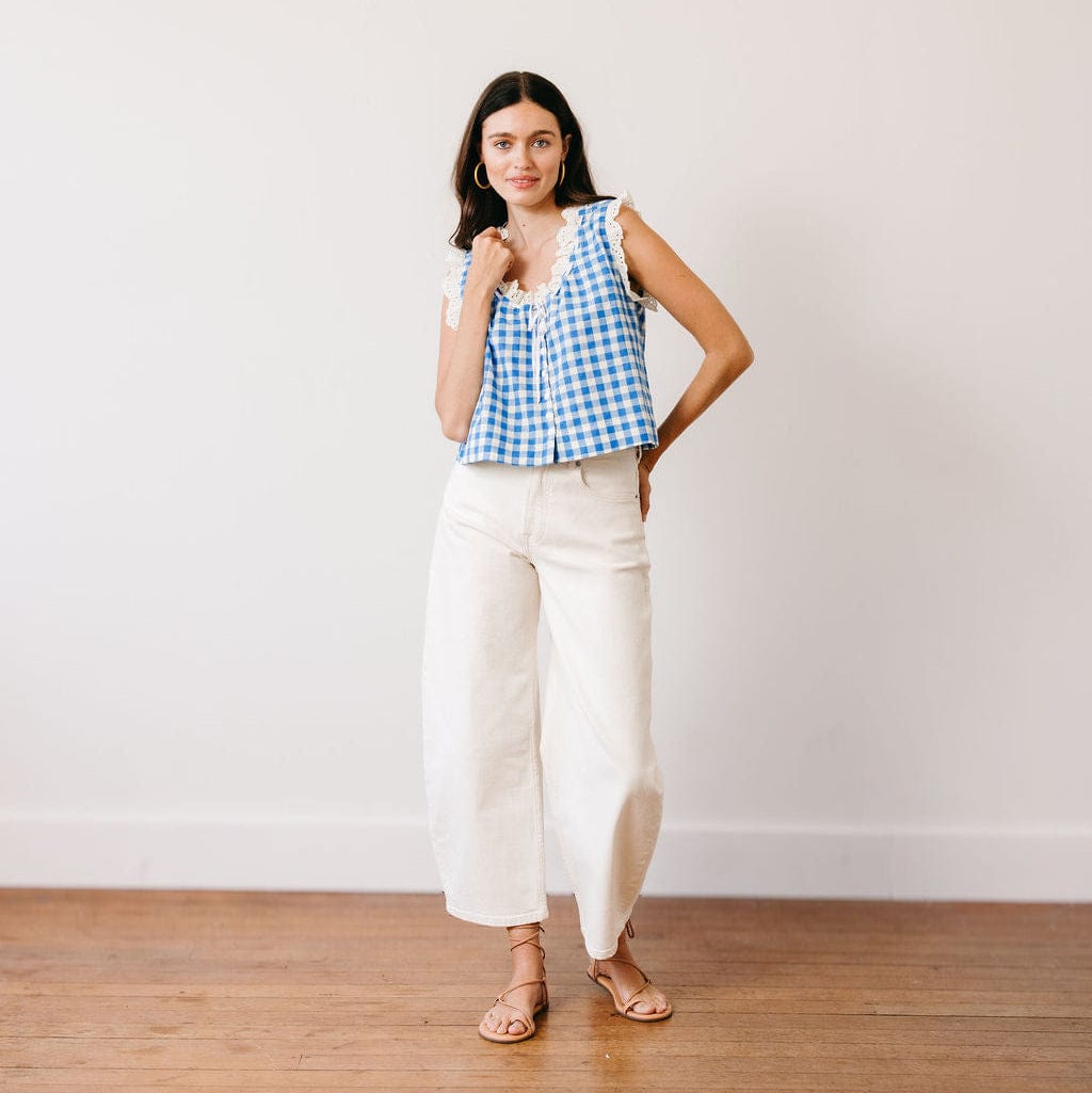 Woman wearing a blue and white checkered top and white pants standing against a plain background