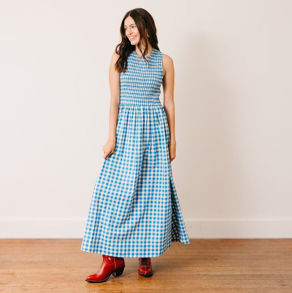 Woman wearing a blue gingham dress with red boots on a wooden floor.