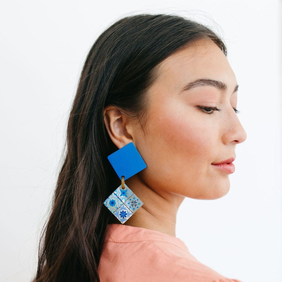 A person wearing blue teja drop earrings with white and blue colors, featuring geometric patterns.