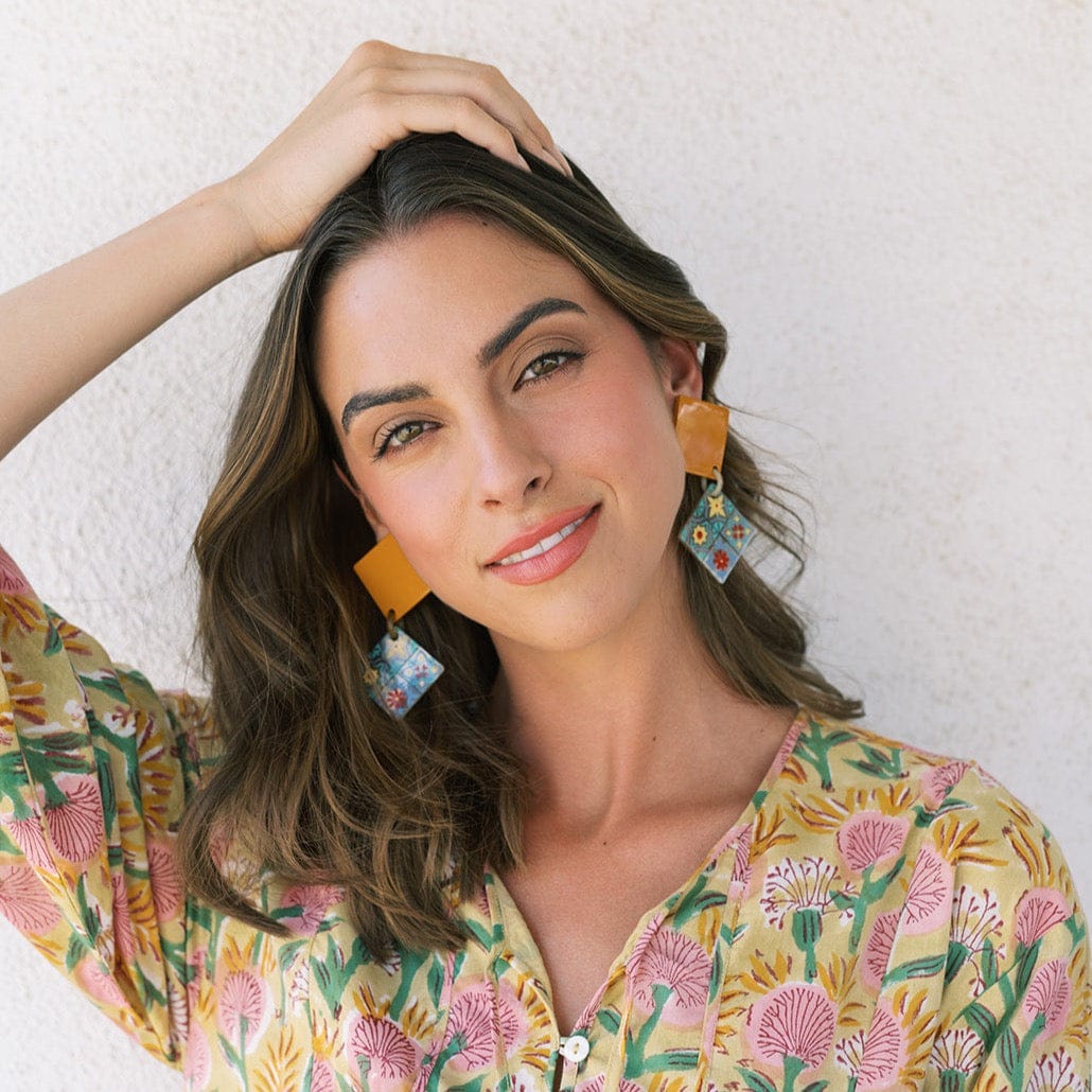 A woman wearing a floral dress and burnt teja drop earrings with multiple colors including white, red, green, yellow, blue, and terracotta.