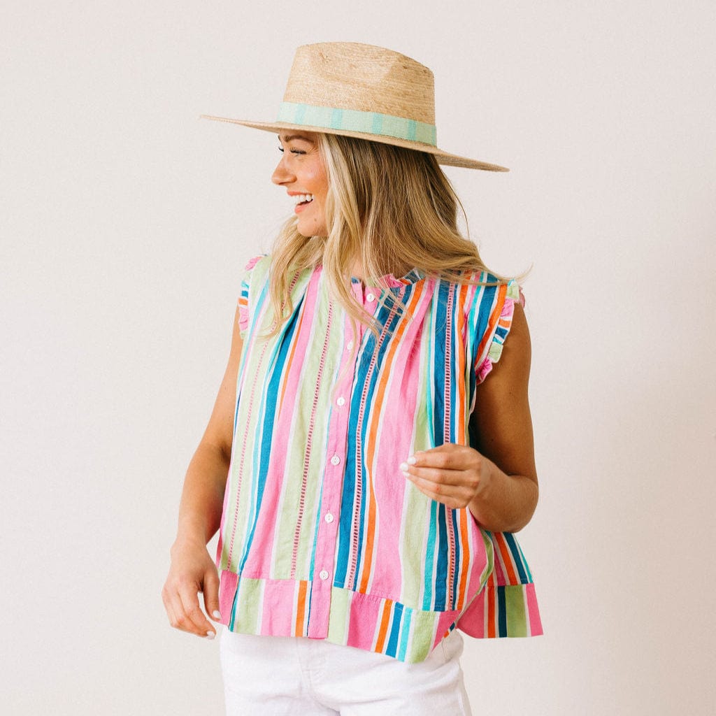 Woman wearing a colorful striped sleeveless top and straw hat on a plain background