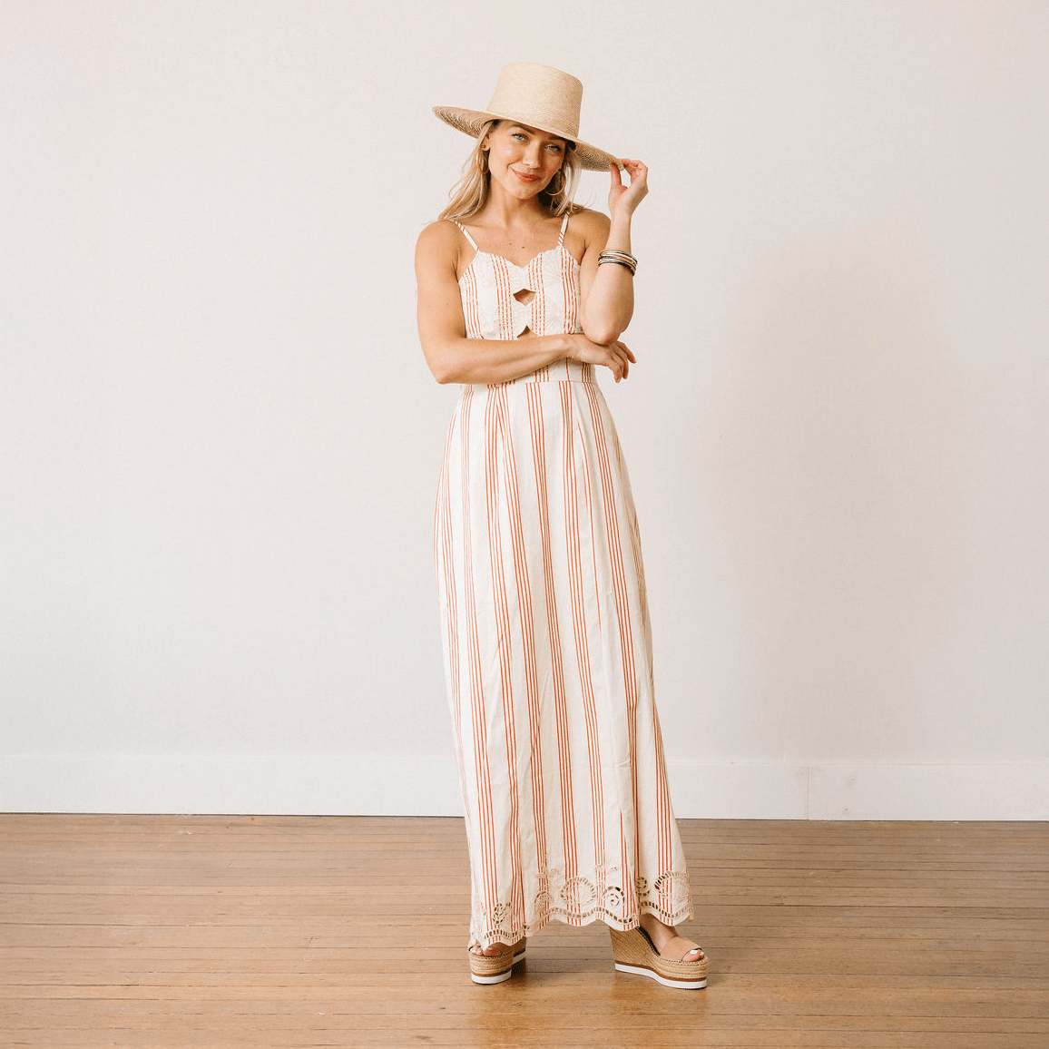 Woman wearing a long striped dress and hat against a plain background