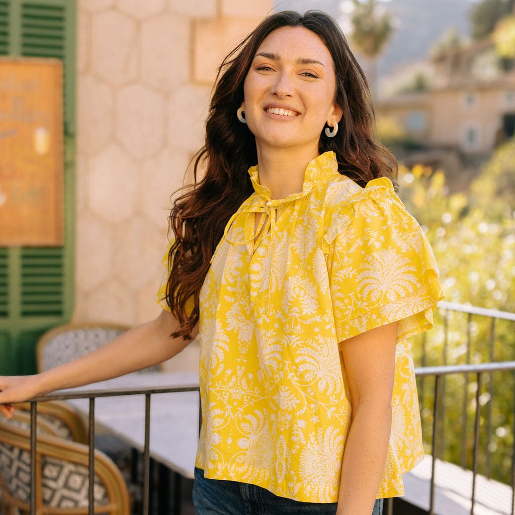 Woman wearing a yellow blouse with floral patterns on a balcony