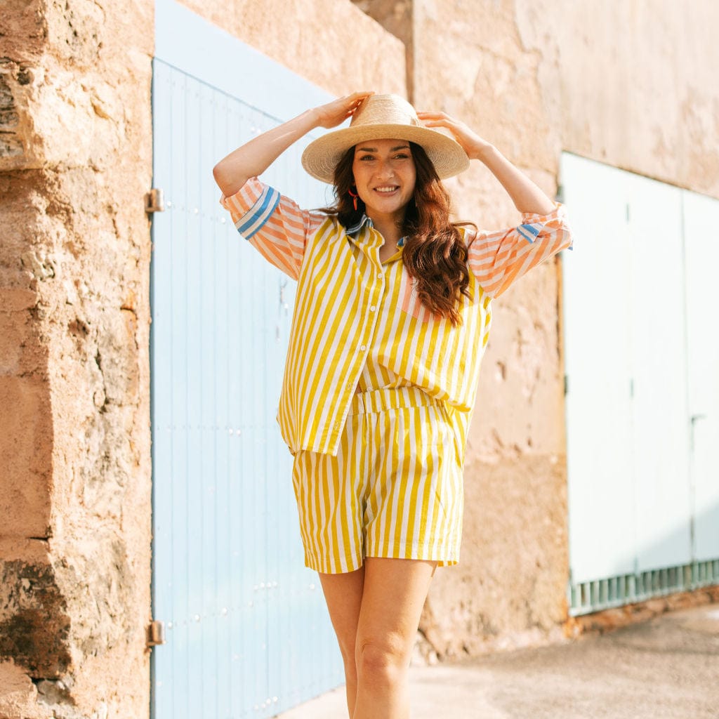Woman in a yellow striped outfit and sun hat standing in front of a stone wall.