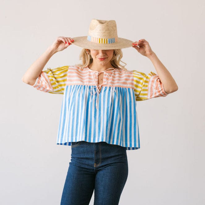 Woman wearing a colorful striped blouse and straw hat against a plain background