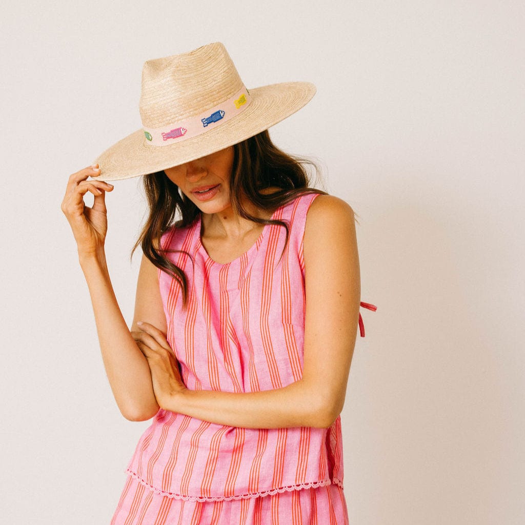 Woman wearing a pink striped dress and straw hat with colorful embellishments on a light background