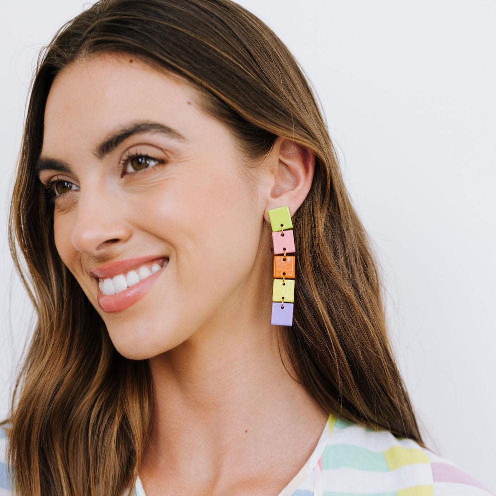 A woman smiling, wearing colorful geometric patterned drop earrings.