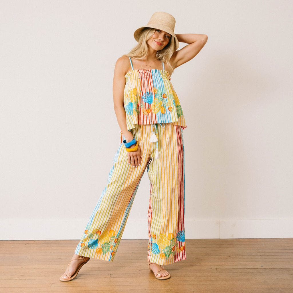 Woman wearing a colorful floral outfit with a straw hat on a wooden floor.