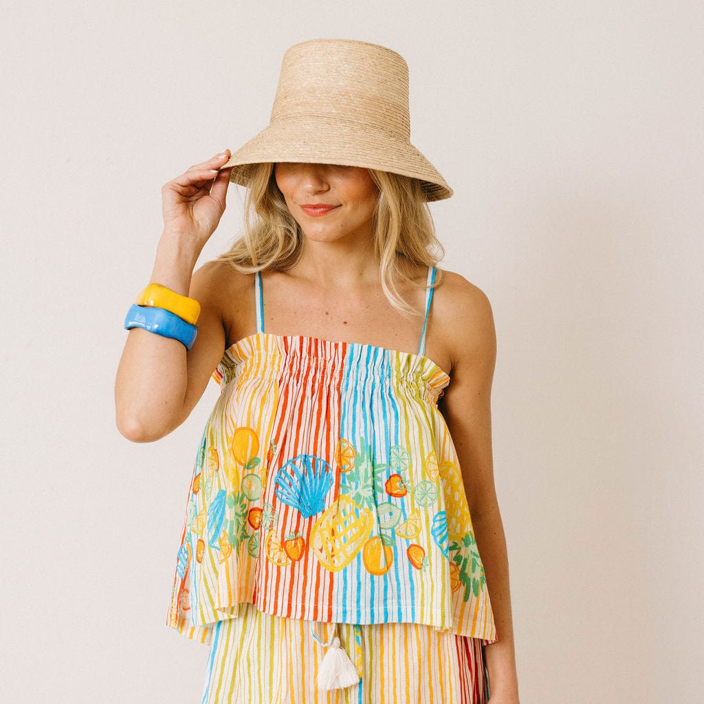 Woman wearing a colorful striped dress with a floral pattern and a straw hat on a plain background