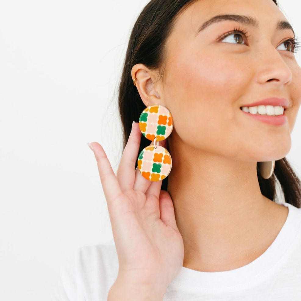 A person showcasing earrings with a geometric pattern in multiple colors including cream, light pink, green, red, and terracotta.