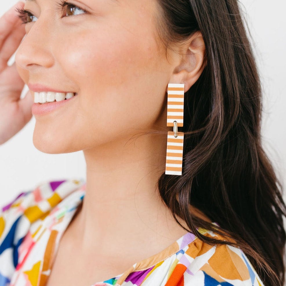 A woman wearing the Isabella Tan Striped Earrings, which are long drop earrings with white and burnt orange stripes.