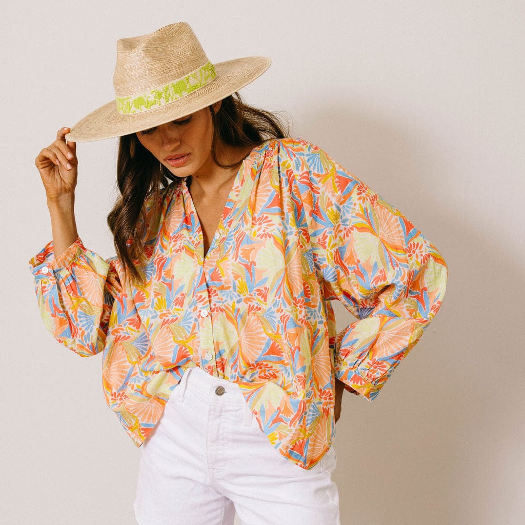 Woman wearing a colorful floral blouse and straw hat against a plain background