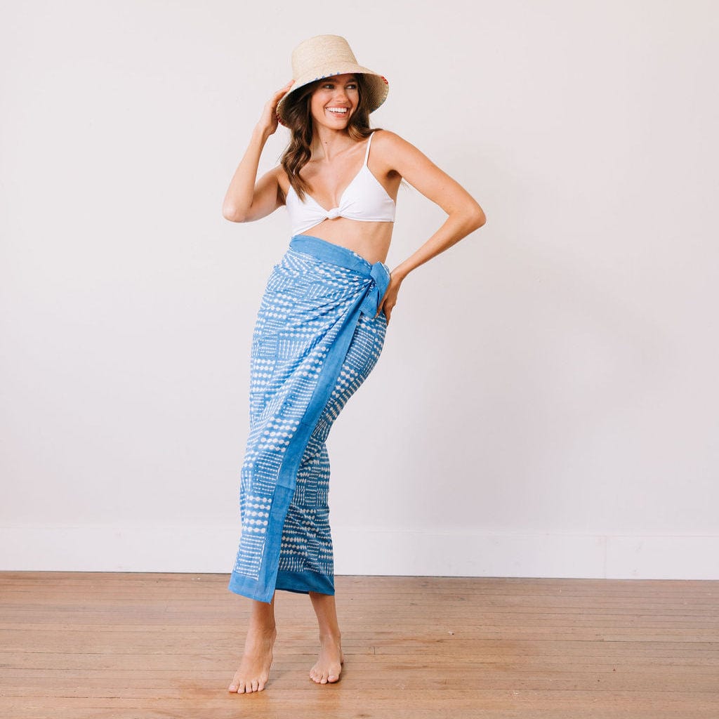 Woman wearing a blue patterned sarong and white bikini top against a plain background