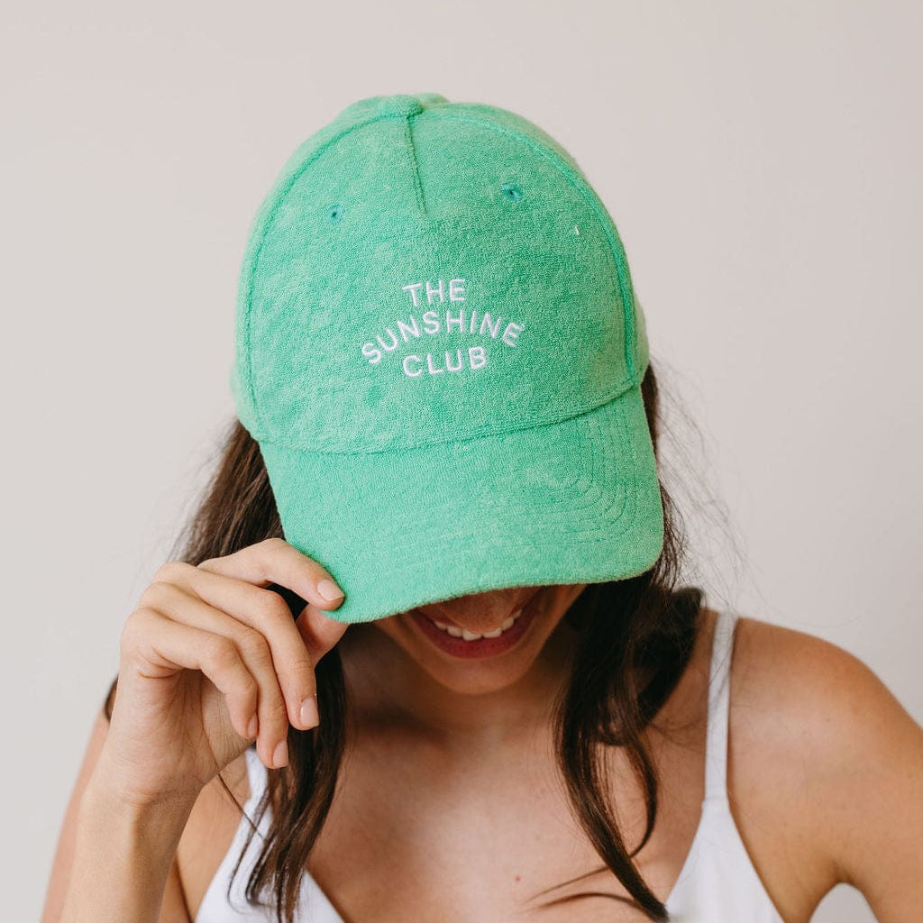 Person wearing a green cap with 'The Sunshine Club' text on a plain background