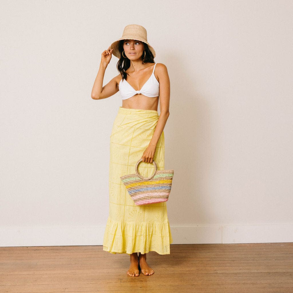 Woman in a yellow skirt and white top holding a colorful bag against a plain background