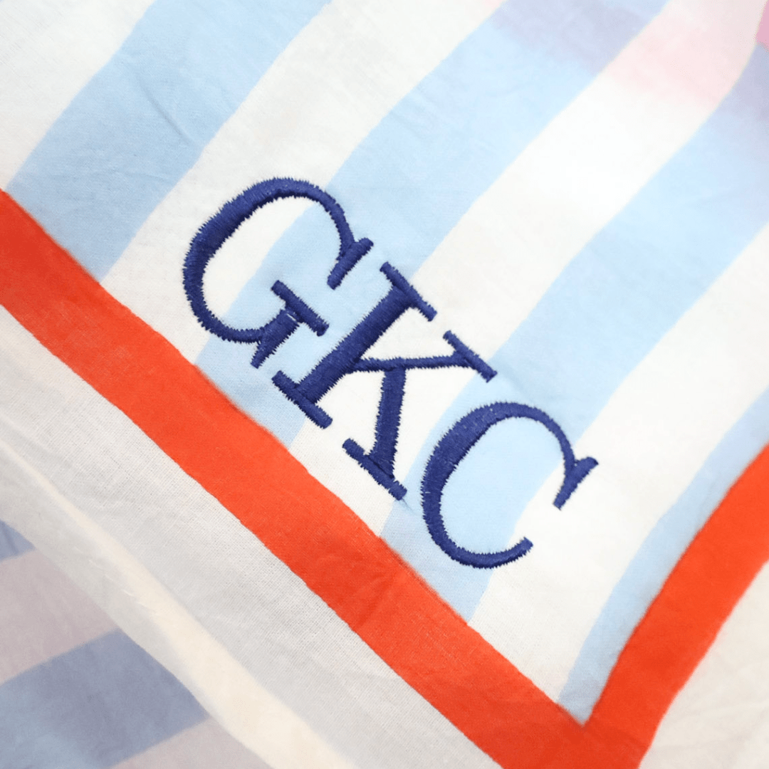 A close-up of a fabric with a striped pattern featuring blue and red stripes, and the letters 'GKC' embroidered in blue.
