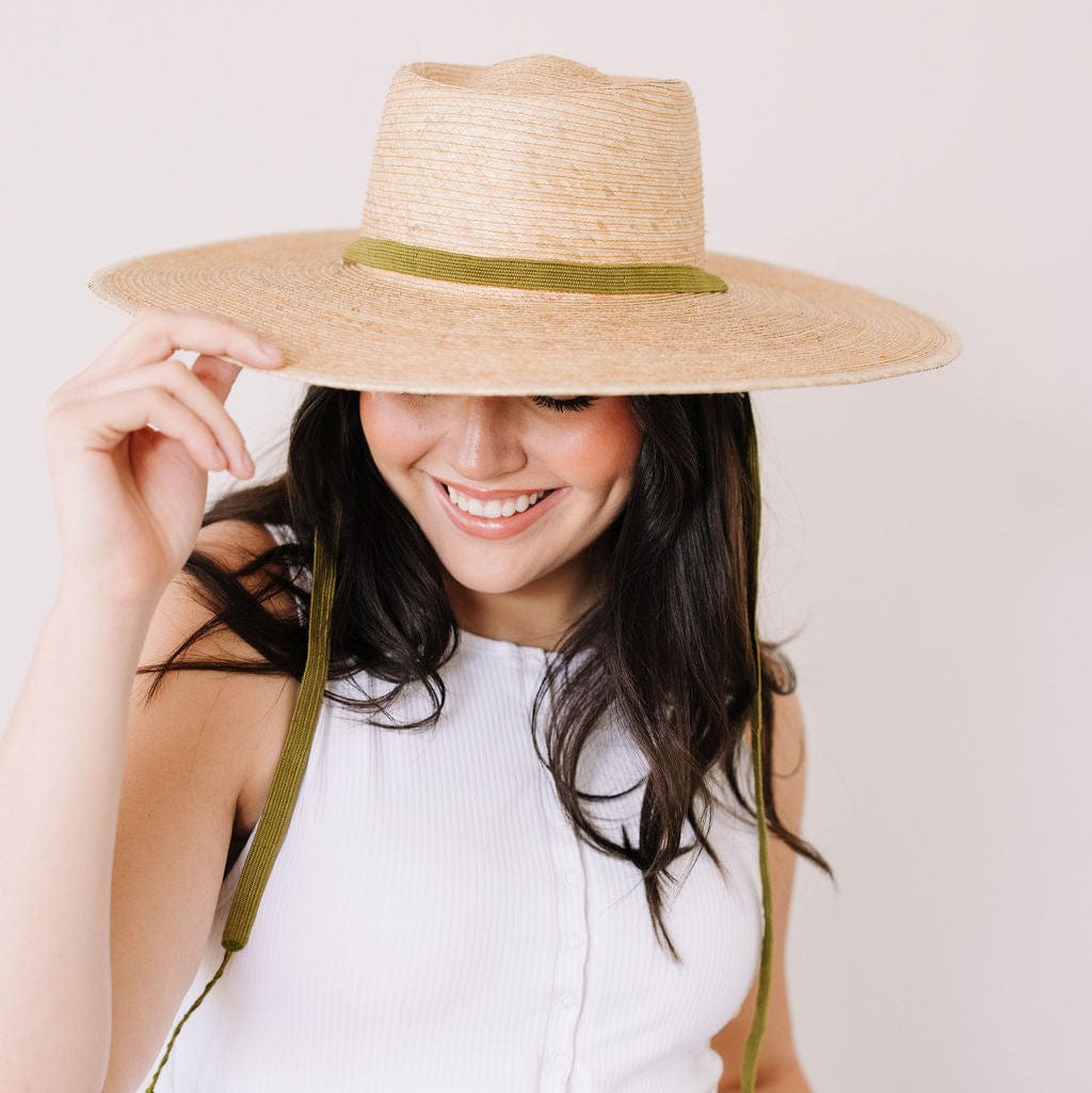 Woman wearing a wide-brimmed straw hat with a green band on a plain background