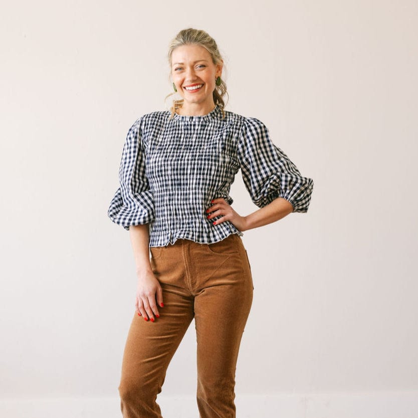 Woman wearing a checkered blouse and brown pants against a plain background
