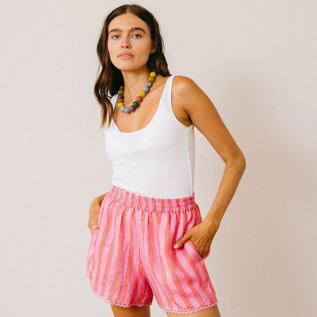 Woman wearing a white tank top and pink striped shorts against a plain background