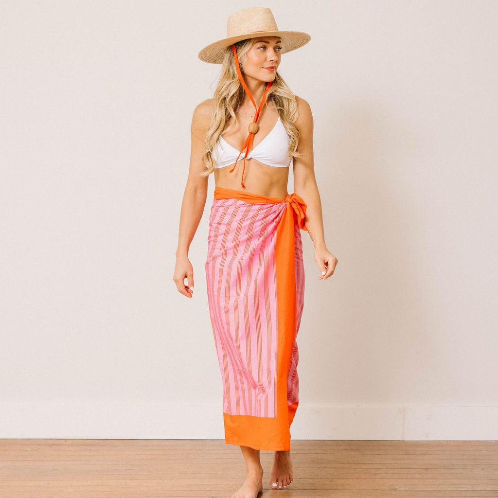 Woman wearing a pink and orange striped sarong with a white bikini top against a plain background