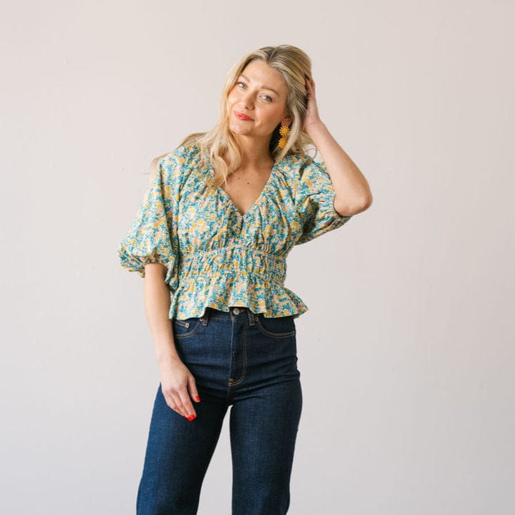 Woman wearing a floral blouse and jeans against a plain background