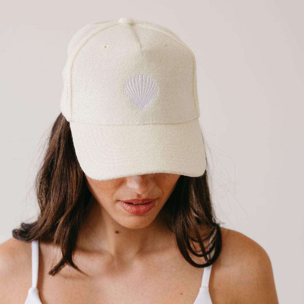 Person wearing a beige cap with a shell emblem on a plain background