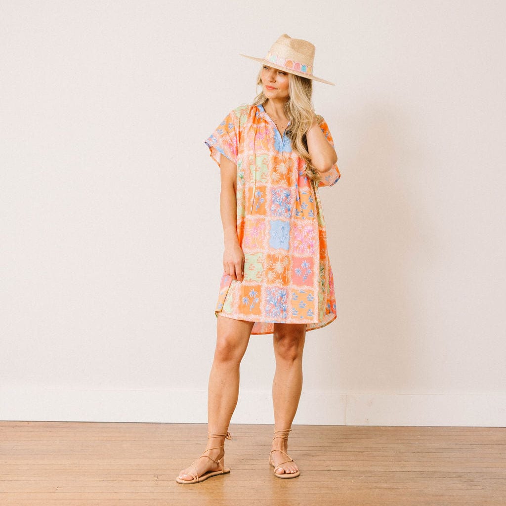 Woman wearing a colorful patchwork dress and straw hat against a plain background