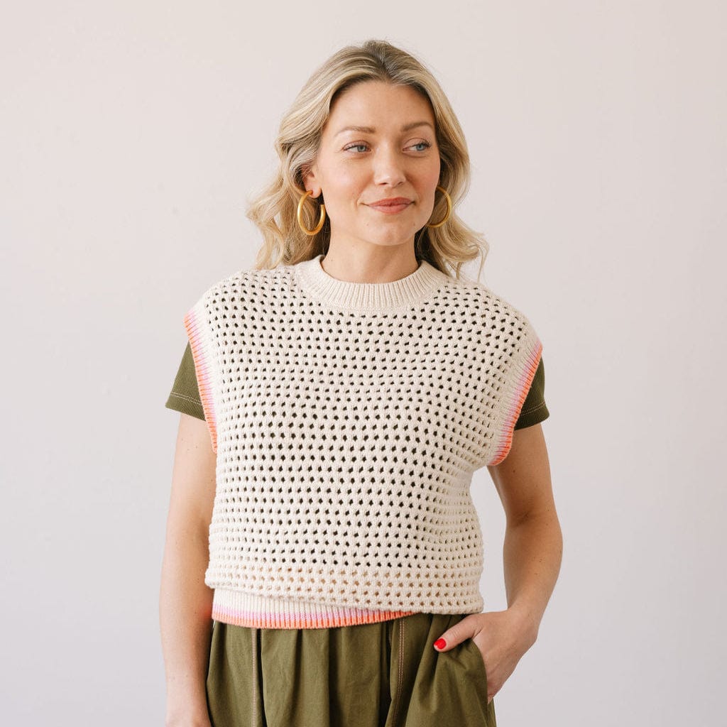 Woman wearing a beige knitted vest over a green shirt on a plain background
