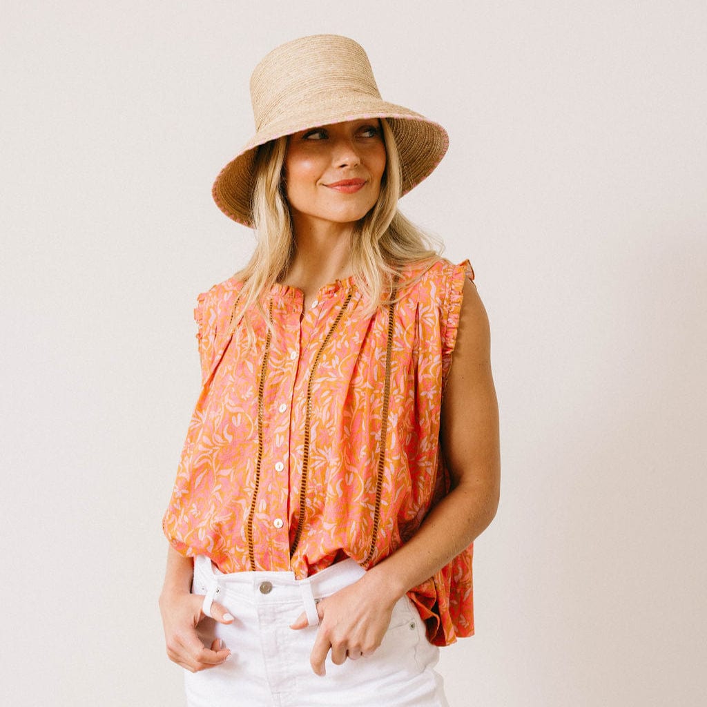 Woman wearing a patterned top and straw hat against a plain background