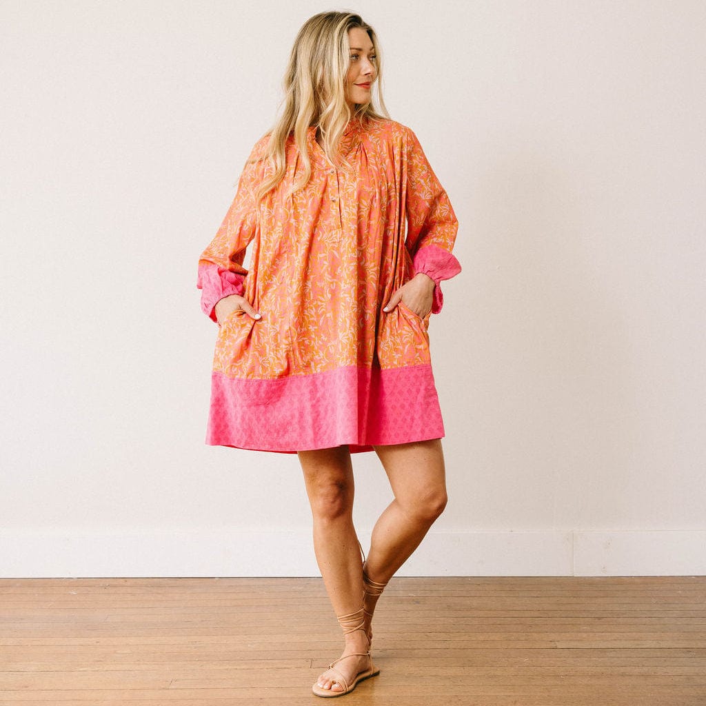 Woman wearing a colorful dress with an orange and pink pattern on a plain background