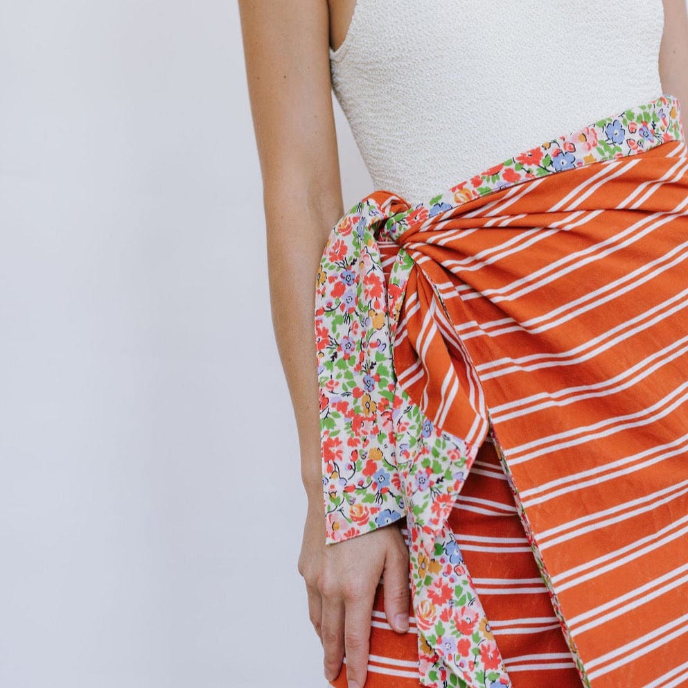 Close-up of a person wearing a white top and an orange sarong with a floral pattern on one side and stripes on the other.