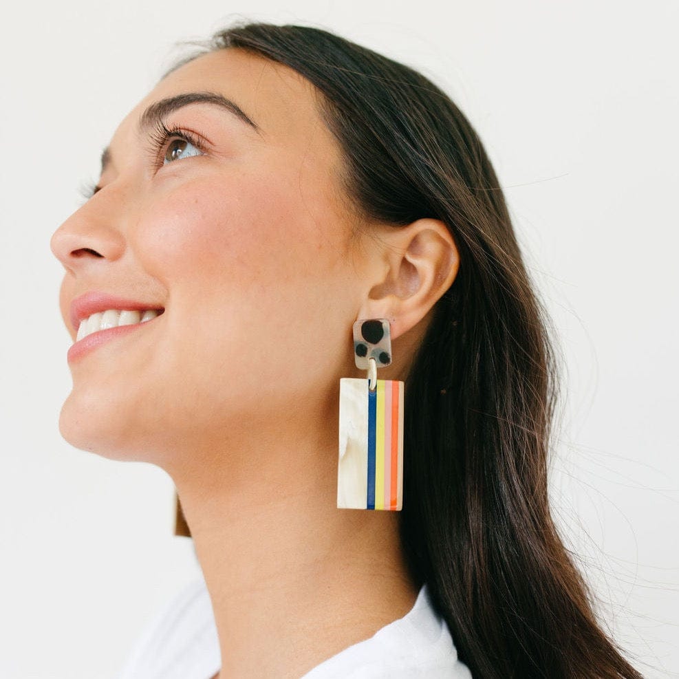 A woman wearing a pair of drop earrings featuring natural and colorful horizontal stripes, made from buffalo horn with stainless steel ear post.