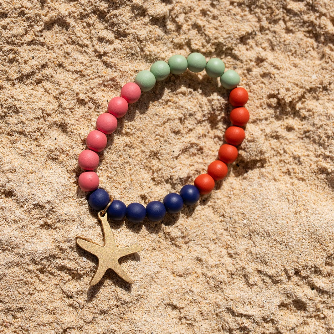 Colorful beaded bracelet with a starfish charm on sandy surface