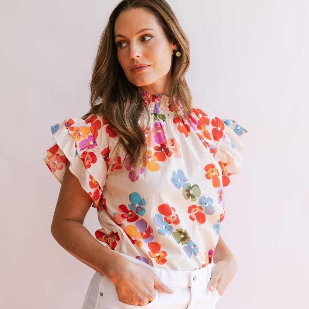 A woman wearing a multicolored floral print top with ruffle sleeves and a ruched mock neckline.