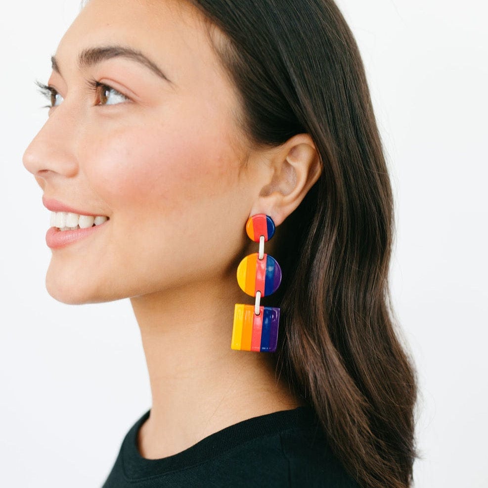 A woman wearing a pair of multicolored striped earrings with tiers in yellow, orange, pink, navy, and purple.