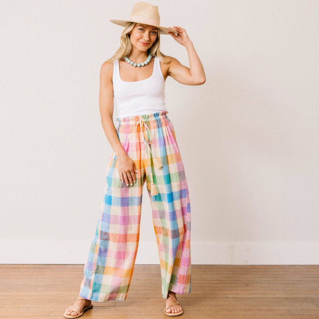Woman wearing a white tank top and colorful plaid pants against a plain background