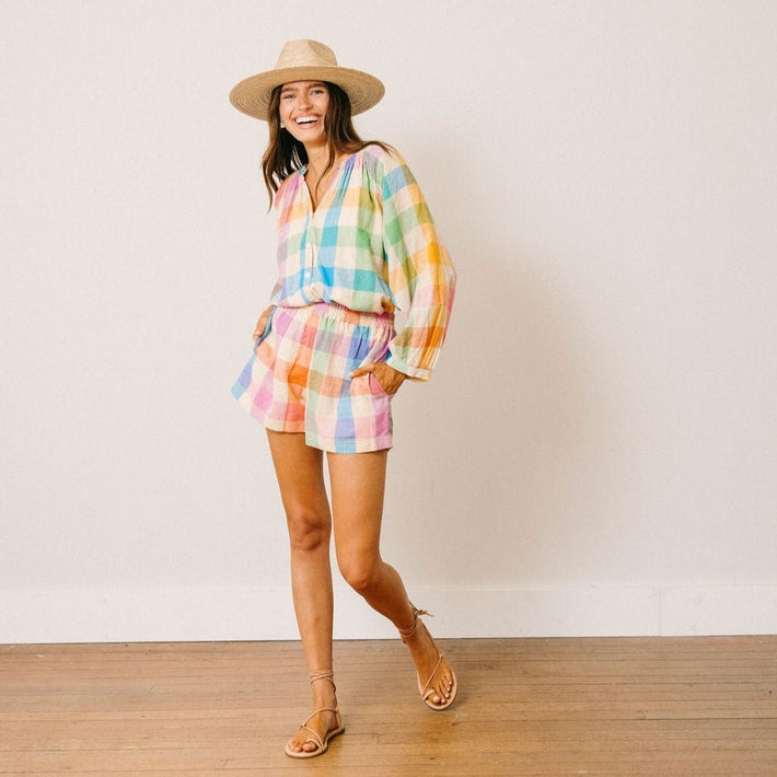 Woman wearing a colorful checkered outfit with a hat on a plain background