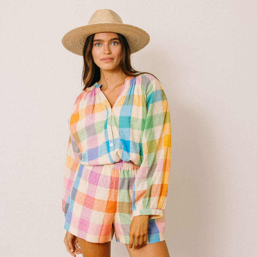 Woman wearing a colorful checkered outfit and straw hat against a plain background