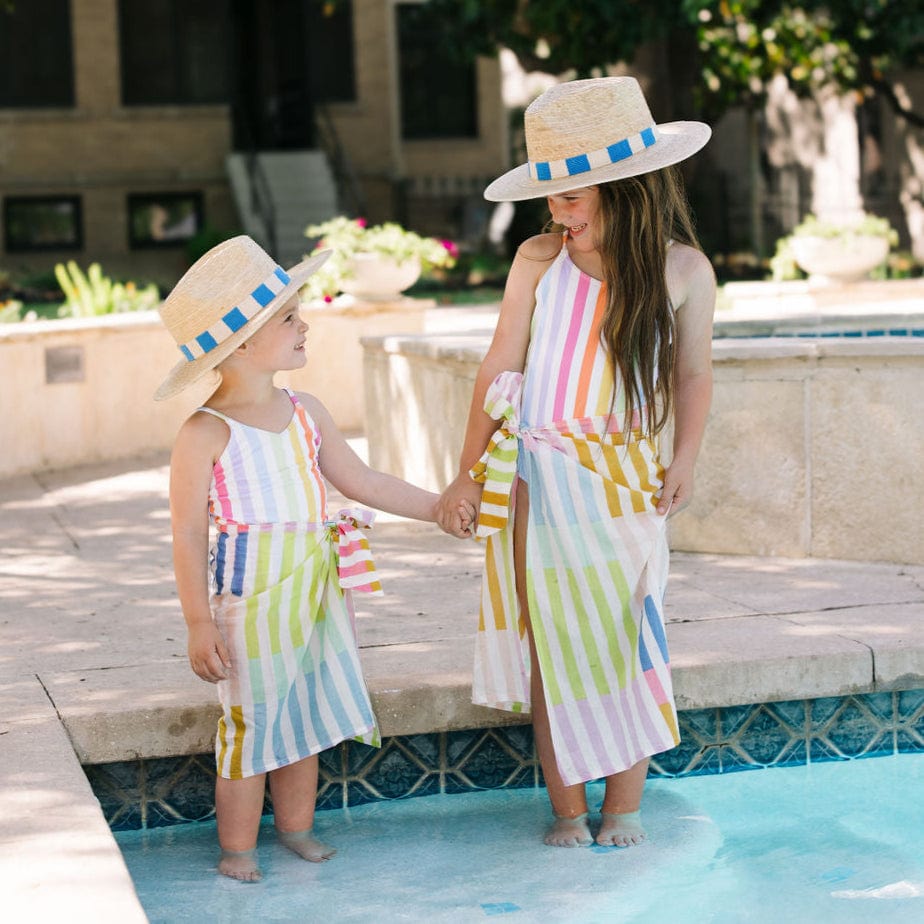 Two children in matching striped dresses and hats by a pool.