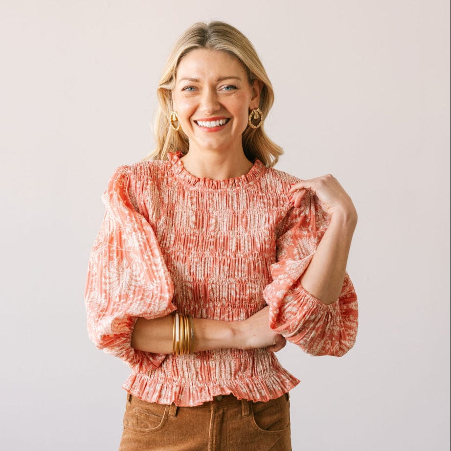 Woman wearing a coral patterned blouse with ruffled sleeves on a plain background