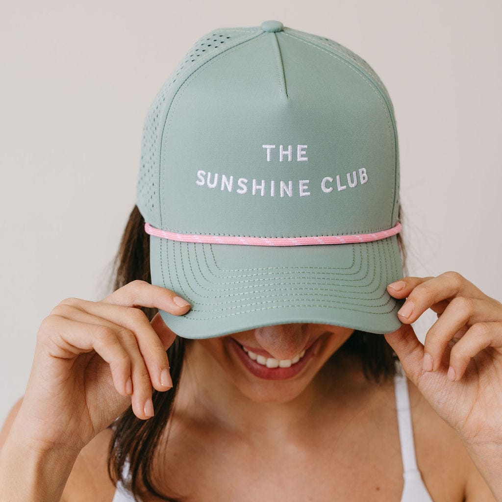 Person wearing a light green cap with 'The Sunshine Club' text on a plain background
