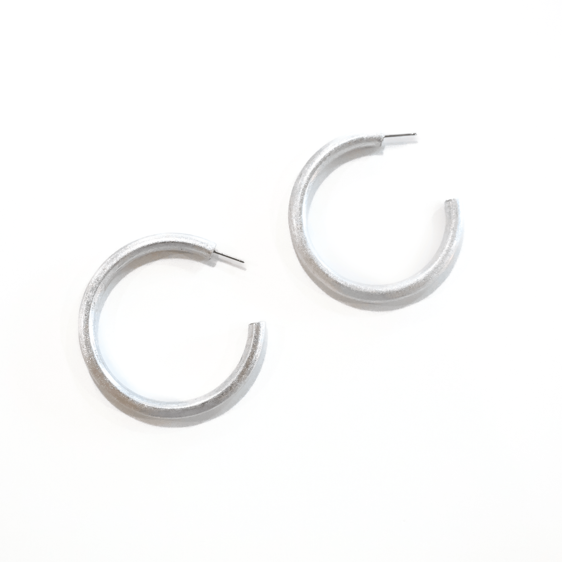 A pair of metallic silver hoop earrings on a white background