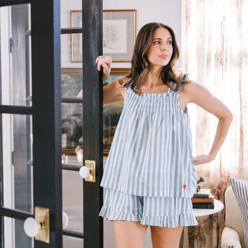 Woman wearing a blue and white striped dress standing in a room with a black door and framed pictures on the wall.