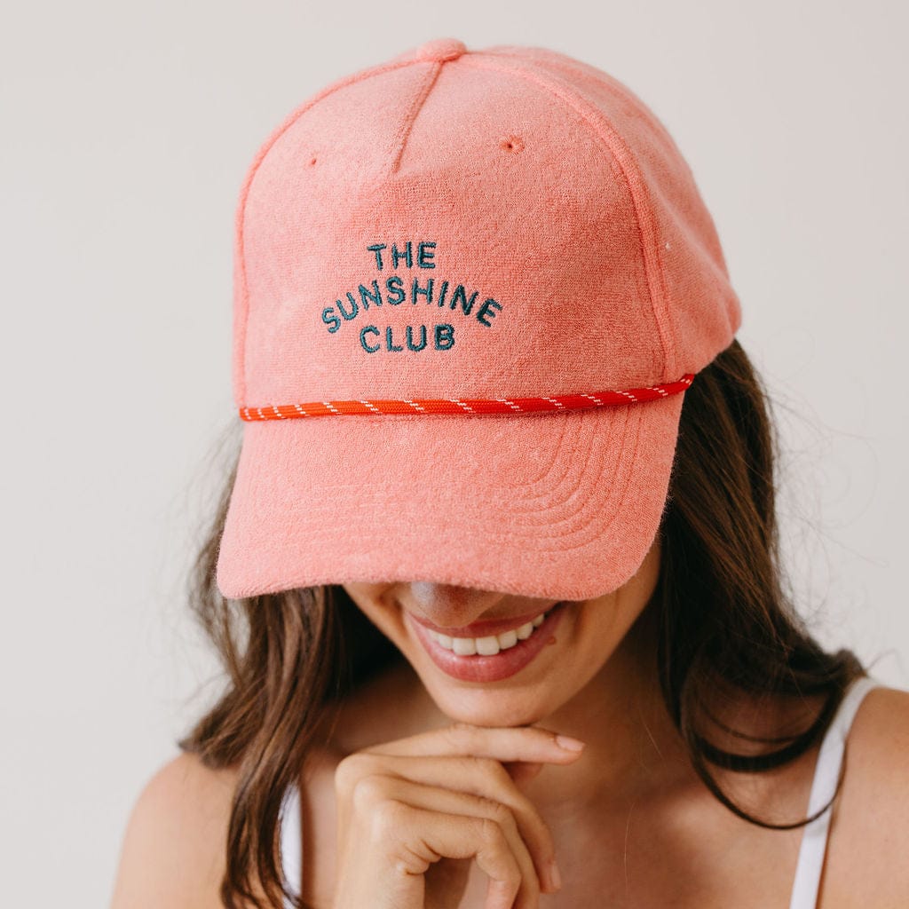 Person wearing a pink cap with 'The Sunshine Club' text on a plain background