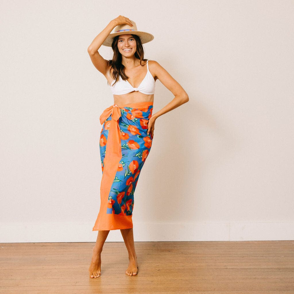 Woman wearing a colorful sarong and white bikini top against a plain background