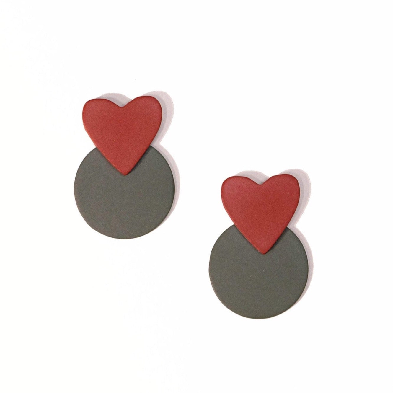 A pair of earrings featuring a red heart shape on top of a dark green circular shape.